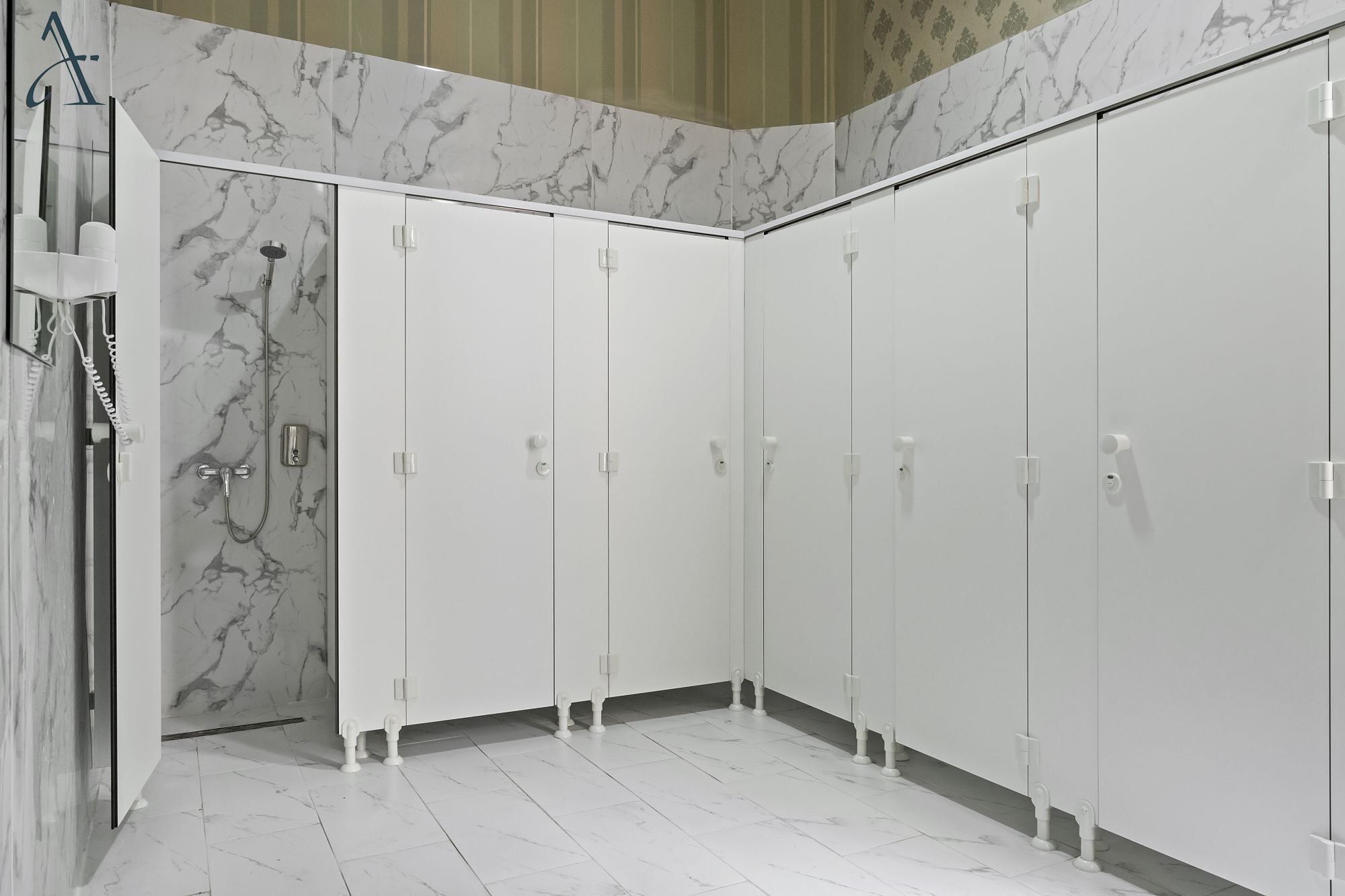 Un baño con paredes de mármol blanco, ducha e inodoro.