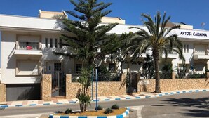 A building with a sign reading "APTOS. CARMINA" and a street in front with a roundabout and palm trees. - Carmina Apartments (Carboneras)