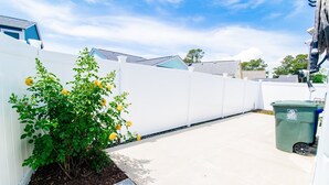 A clean, white-fenced outdoor area with a plant and a green trash bin. - Flamingo Hideaway Modern House w Elevator (North Myrtle Beach)