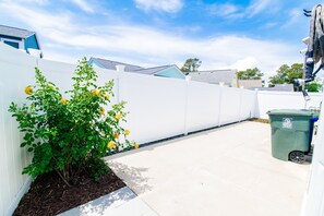 A clean, white-fenced outdoor area with a plant and a green trash bin.