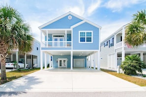 A two-story residential building with a balcony, a garage, and a driveway. - Flamingo Hideaway Modern House w Elevator (North Myrtle Beach)