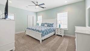 A bedroom with a bed, nightstands, a dresser, a ceiling fan, and windows.
