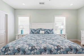 A bedroom with a bed, two nightstands, a window with blinds, and a door. - Flamingo Hideaway Modern House w Elevator (North Myrtle Beach)