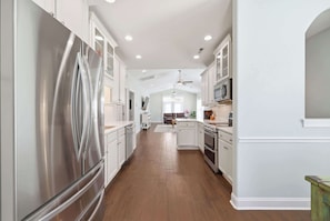 A kitchen with white cabinets, stainless steel appliances, and a wooden floor. - Flamingo Hideaway Modern House w Elevator (North Myrtle Beach)