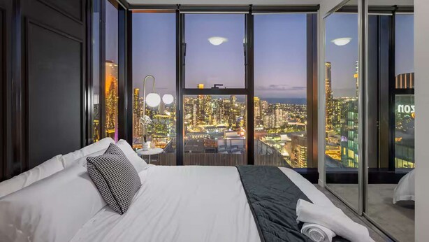 Ein modernes Hotelzimmer mit einem großen Bett und Blick auf eine Stadtlandschaft im Abenddämmerung, mit großen Fenstern.