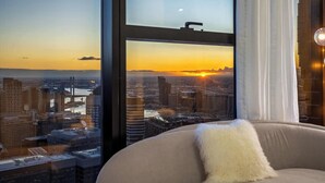 Ein Zimmer mit großem Fenster und Blick auf die Stadt bei Sonnenuntergang.