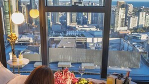 Ein Bett mit Blick auf die Stadt, ein Frühstücksbrett und eine Weinflasche.