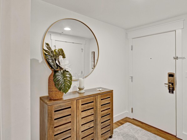 Ein Holzkabinett mit Spiegel, Blumentopf und Kerze an einer weißen Wand.
