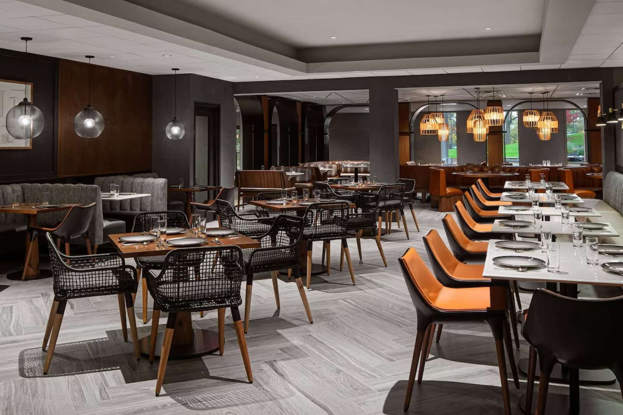 Een modern restaurant met een combinatie van zitbankjes en tafels, uitgevoerd in een neutrale kleurenpalet en met een eigentijdse inrichting.