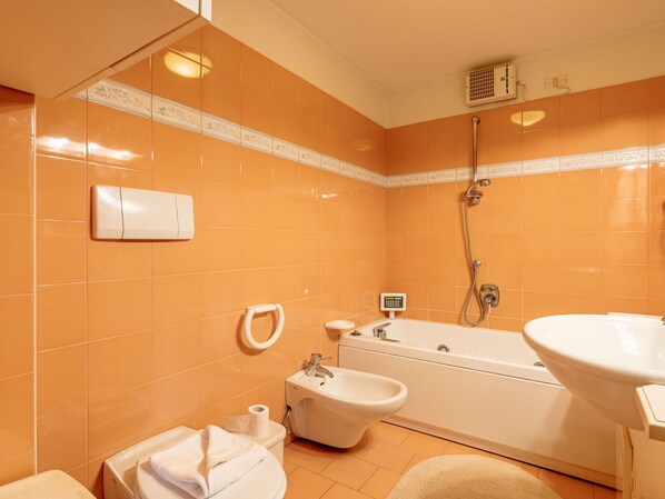 Een badkamer met oranje tegels, een bad, een bidet en een toilet.