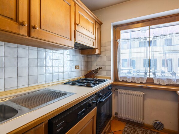 Una cocina con armarios de madera, estufa a gas, lavavajillas y una ventana con cortinas de encaje.