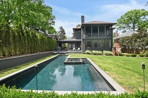 A modern house with a swimming pool, a covered patio, and a well-maintained lawn.