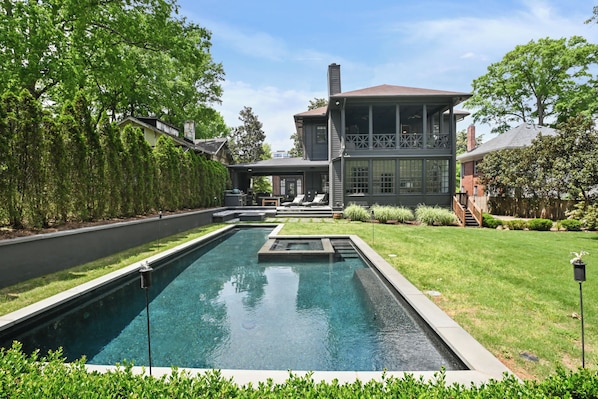A modern house with a swimming pool, a covered patio, and a well-maintained lawn.