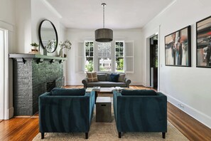 Ein Wohnzimmer mit Kamin, einer Couch, zwei Sesseln, einem Couchtisch und Kunstwerken an den Wänden.