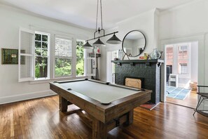A pool table in a room with large windows, a fireplace, and a mirror on the wall.