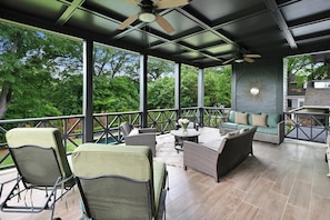A covered outdoor patio with wicker furniture, a ceiling fan, and a decorative sunburst wall piece.