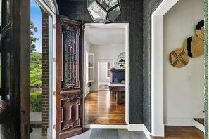 A wooden door with intricate carvings leading to a room with a dark wall and a round mirror.