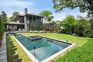 Ein zweistöckiges Haus mit einem großen rechteckigen Pool im Garten.