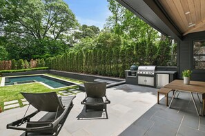 Um pátio externo com piscina, cadeiras de descanso, mesa de jantar e área de churrasco.