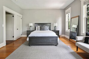 A bedroom with a large bed, two bedside tables with lamps, a dresser, a chair, and a mirror.