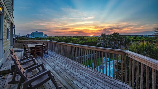 En træterrasse med pool, der kigger ud over et frodigt landskab og en solnedgang.