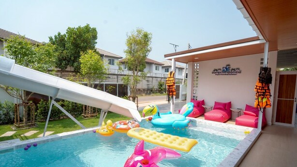 A swimming pool with inflatable toys, a slide, and lounge chairs. - Ongsa Poolvilla Udonthani (Udon Thani)