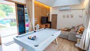 A modern living room with a pool table, a sofa, and a television. - Ongsa Poolvilla Udonthani (Udon Thani)