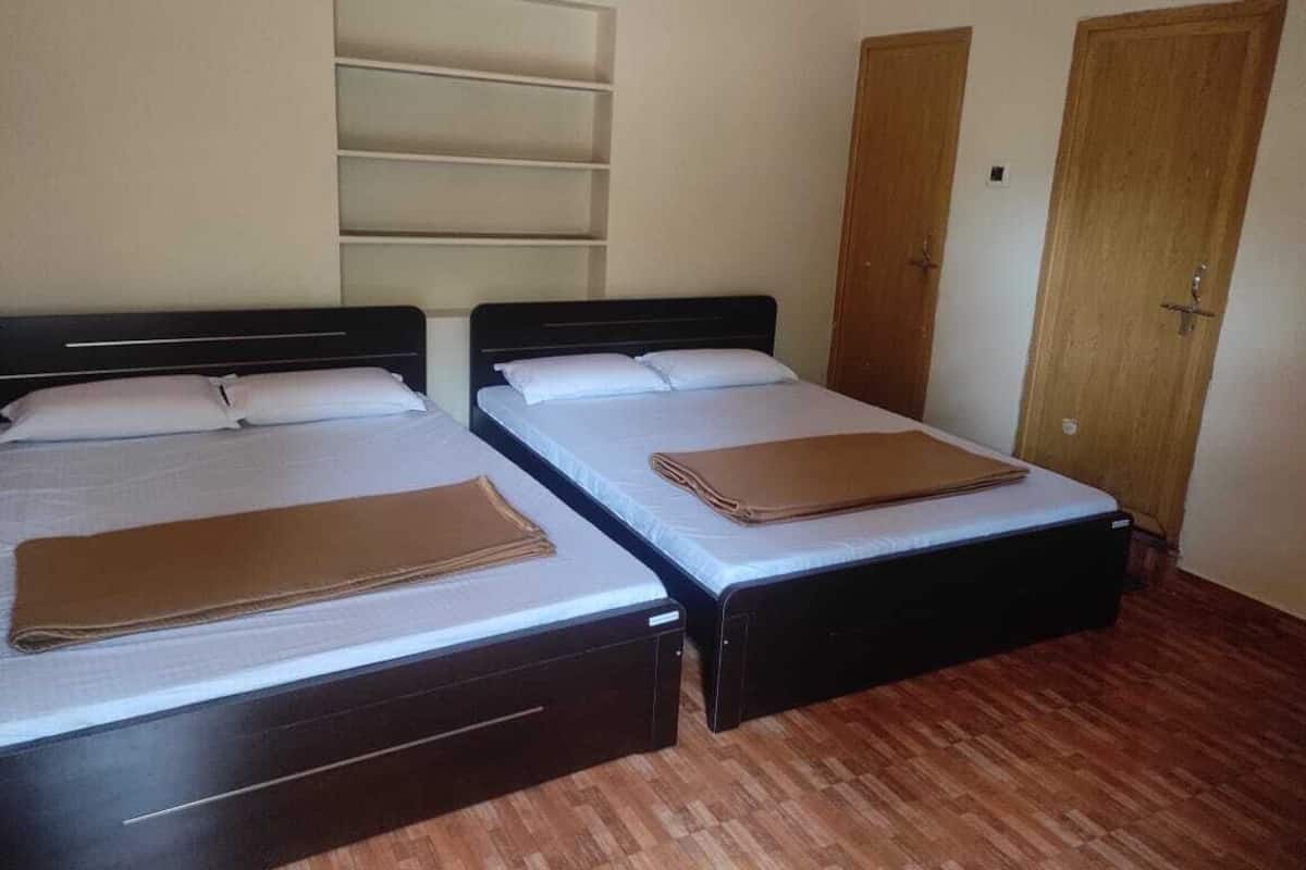 Two single beds with wooden frames and white bedding, a wooden door, and a wall-mounted shelf unit.
