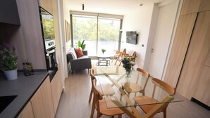 A modern kitchen with a built-in oven, a dining area with a glass table and wooden chairs, and a large sliding glass door leading to a balcony.
