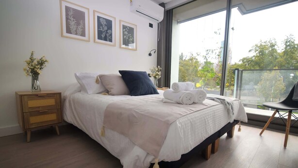 A bedroom with a bed, bedside table, and a view of the outdoors.