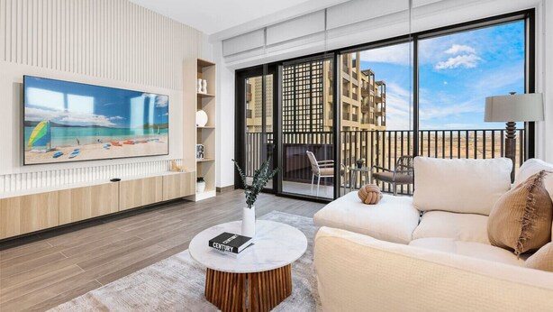 Een moderne woonkamer met een grote flatscreen televisie, een bank, een salontafel en een balkon met uitzicht op gebouwen en de lucht.