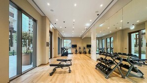 Een ruime fitnessruimte met trainingsapparatuur, grote ramen en een houten vloer.