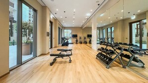 A spacious gym with exercise equipment, large windows, and a wooden floor.