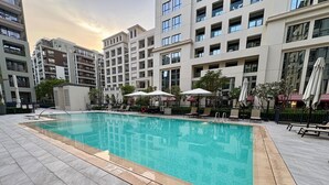 A swimming pool with a tiled deck, surrounded by modern buildings and outdoor seating.