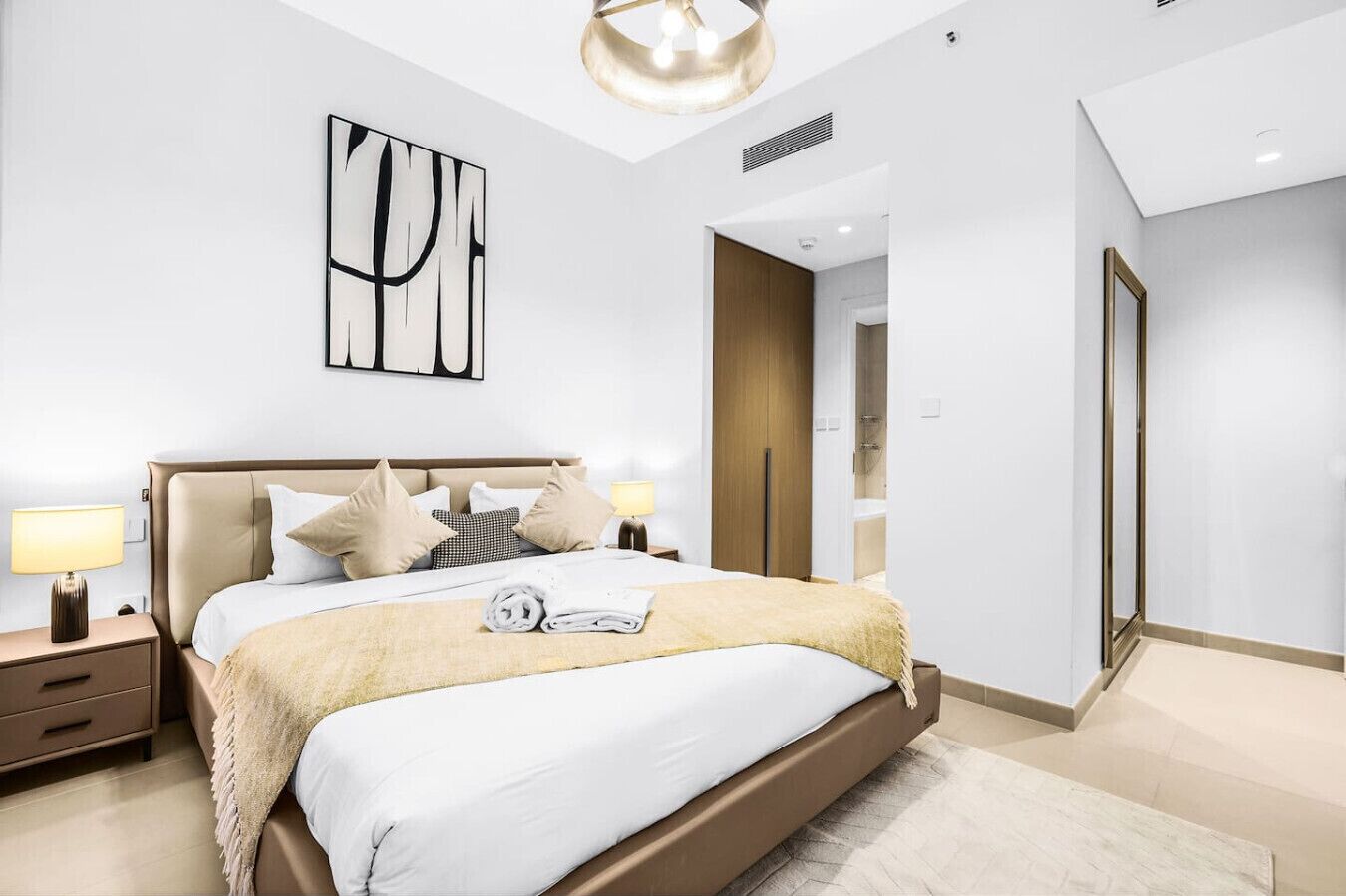 A modern bedroom with a large bed, bedside lamps, a ceiling light, and a wooden door.