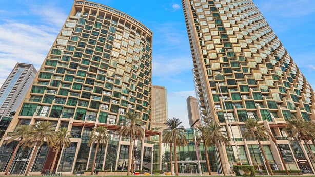 Un hôtel de grande hauteur à la façade incurvée, doté de grandes fenêtres et bordé de palmiers au premier plan.