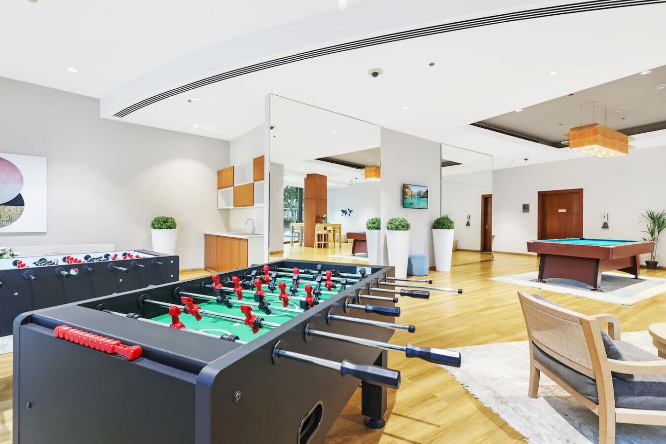 Uma área de lazer interna moderna, com mesa de pebolim, mesa de bilhar e assentos confortáveis.