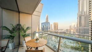 Un balcon avec une table ronde en bois et des chaises, des plantes en pot et une vue sur la ville, notamment sur les grands immeubles.