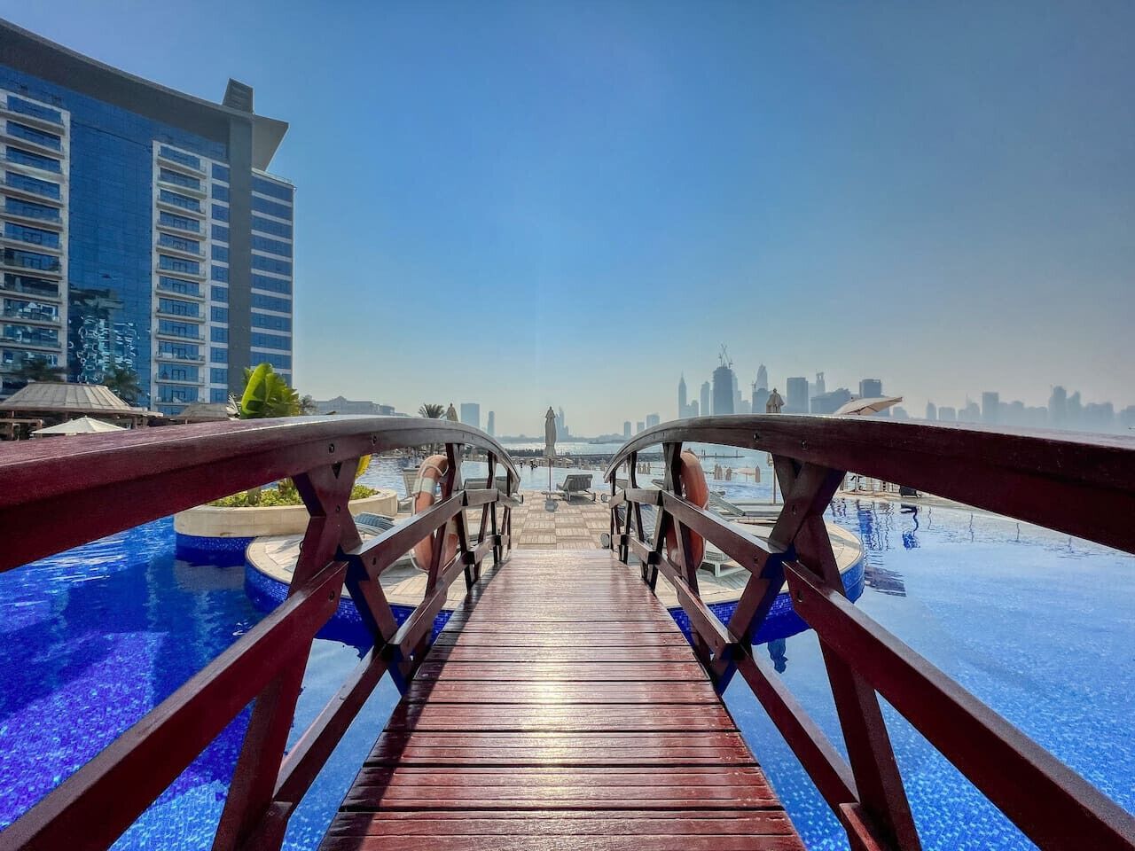Un puente de madera que conduce a una piscina con el horizonte de una ciudad al fondo.