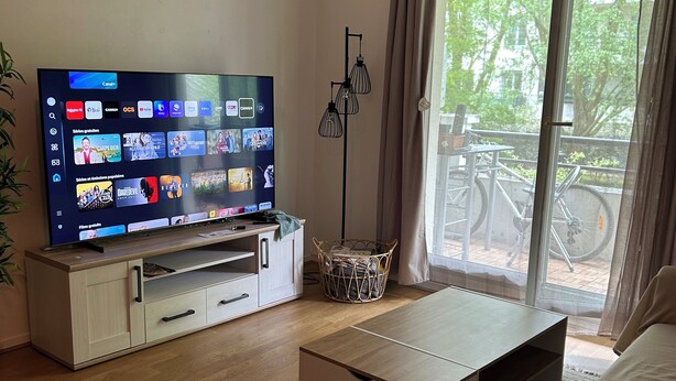 A modern living room with a flat-screen TV, a sofa, a coffee table, and a wicker basket. - Charming T2 on the edge of the Seine with terrace (Mantes-la-Jolie)