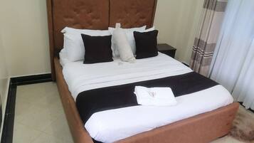 Una cama bien hecha con tablero de cabecera marrón, almohadas blancas y negras, y una manta blanca con una toalla encima.
