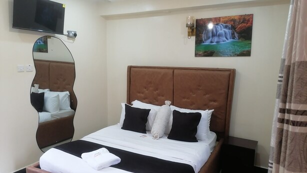 Habitación de hotel ordenada con una cama grande, un televisor montado, un espejo en la pared y un cuadro de una cascada.
