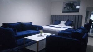 Una sala de estar moderna con un sofá azul, una mesita de centro blanca y una cama con ropa de cama azul.