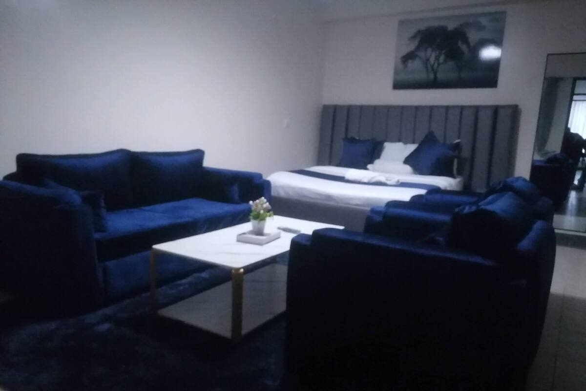 Een moderne woonkamer met een blauwe zithoek, een witte salontafel en een bed met blauw bedlinnen.