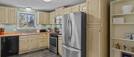 A modern kitchen with light wood cabinets, stainless steel appliances, and a dishwasher.