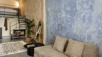 A modern living room with a sofa, a coffee table, a potted plant, and a staircase.