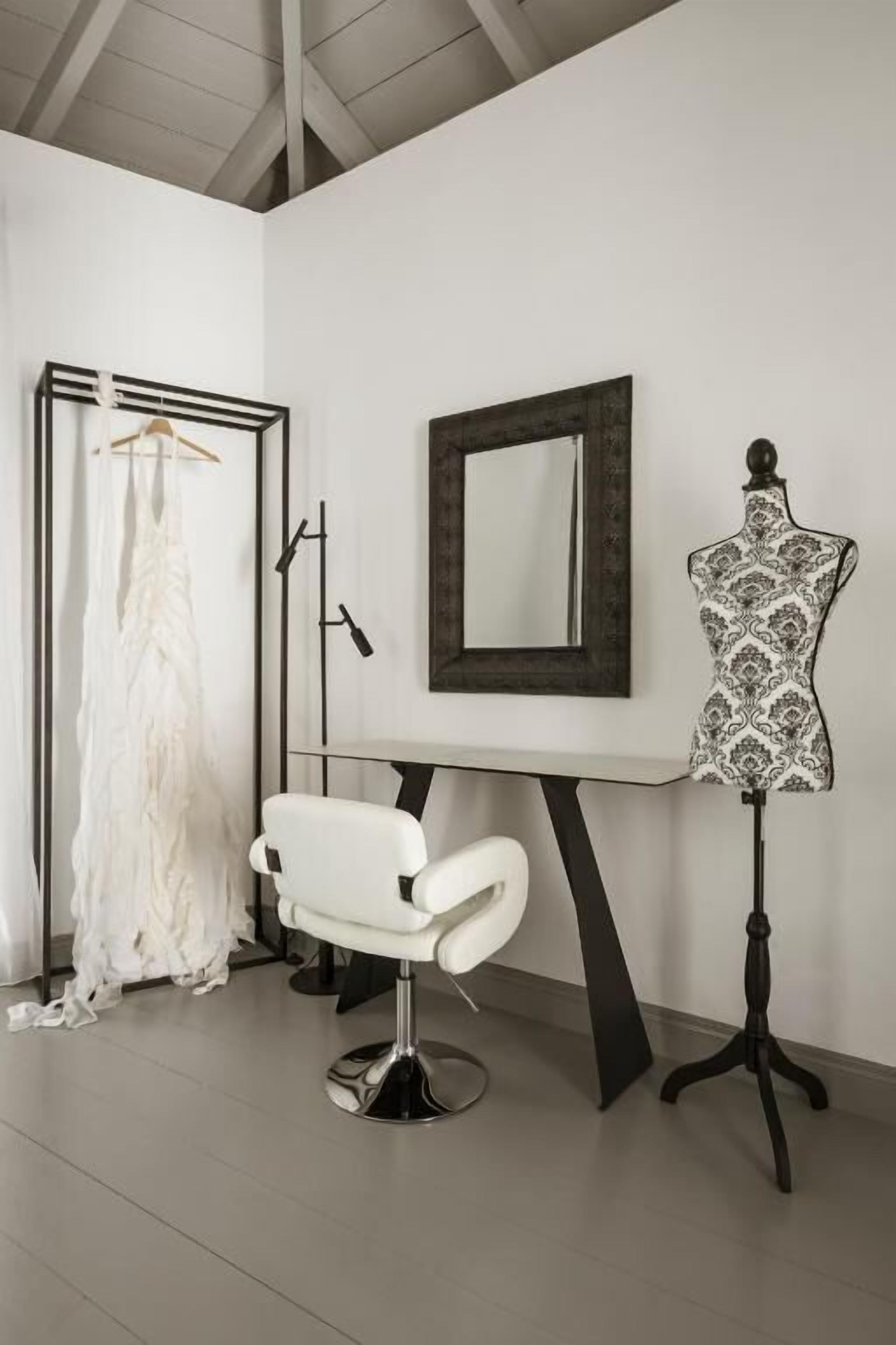 Una habitación con una silla blanca, un maniquí, un espejo y un vestido colgado.