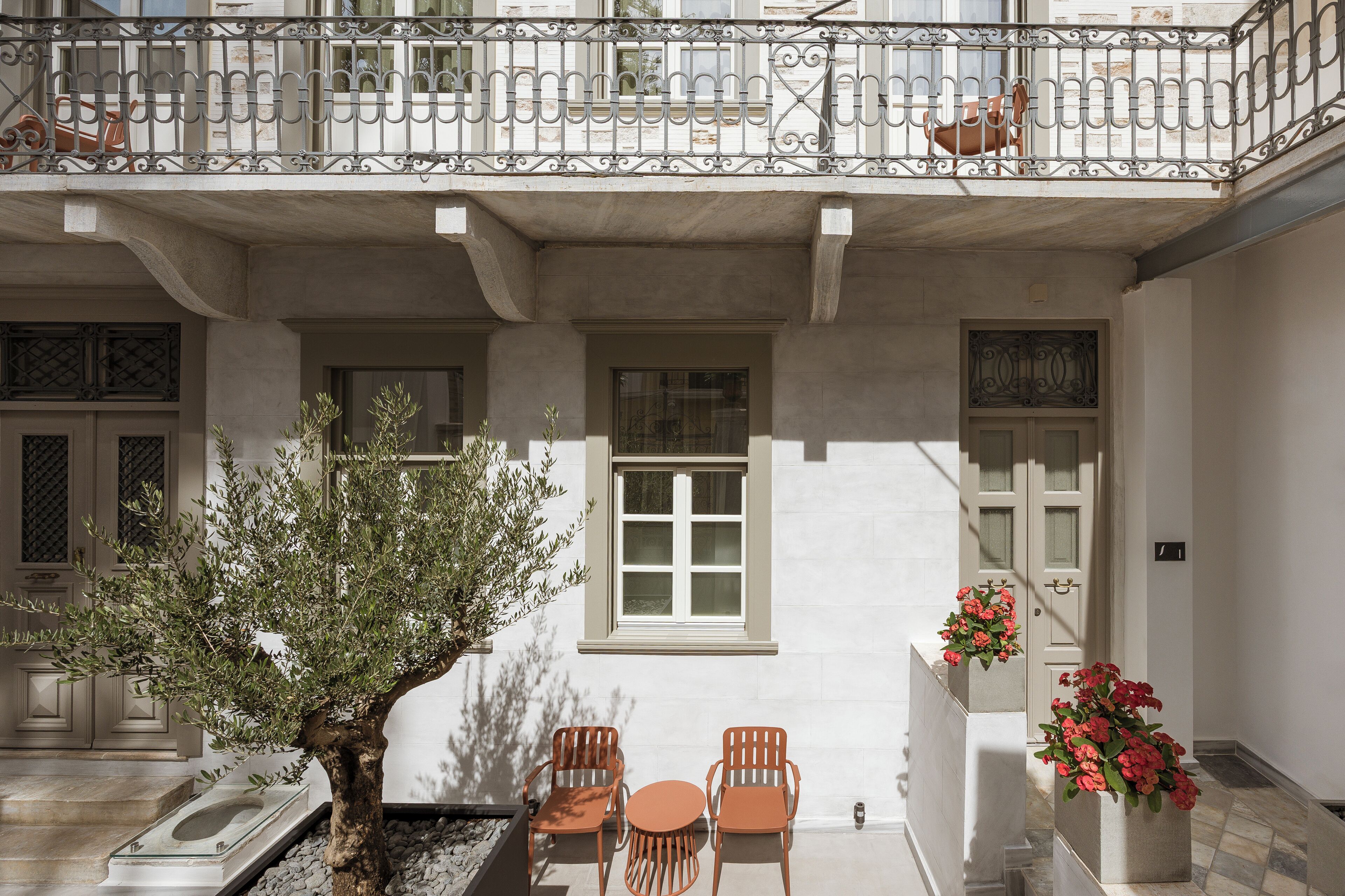 A balcony with wrought iron railings, a potted tree, and two wooden chairs.