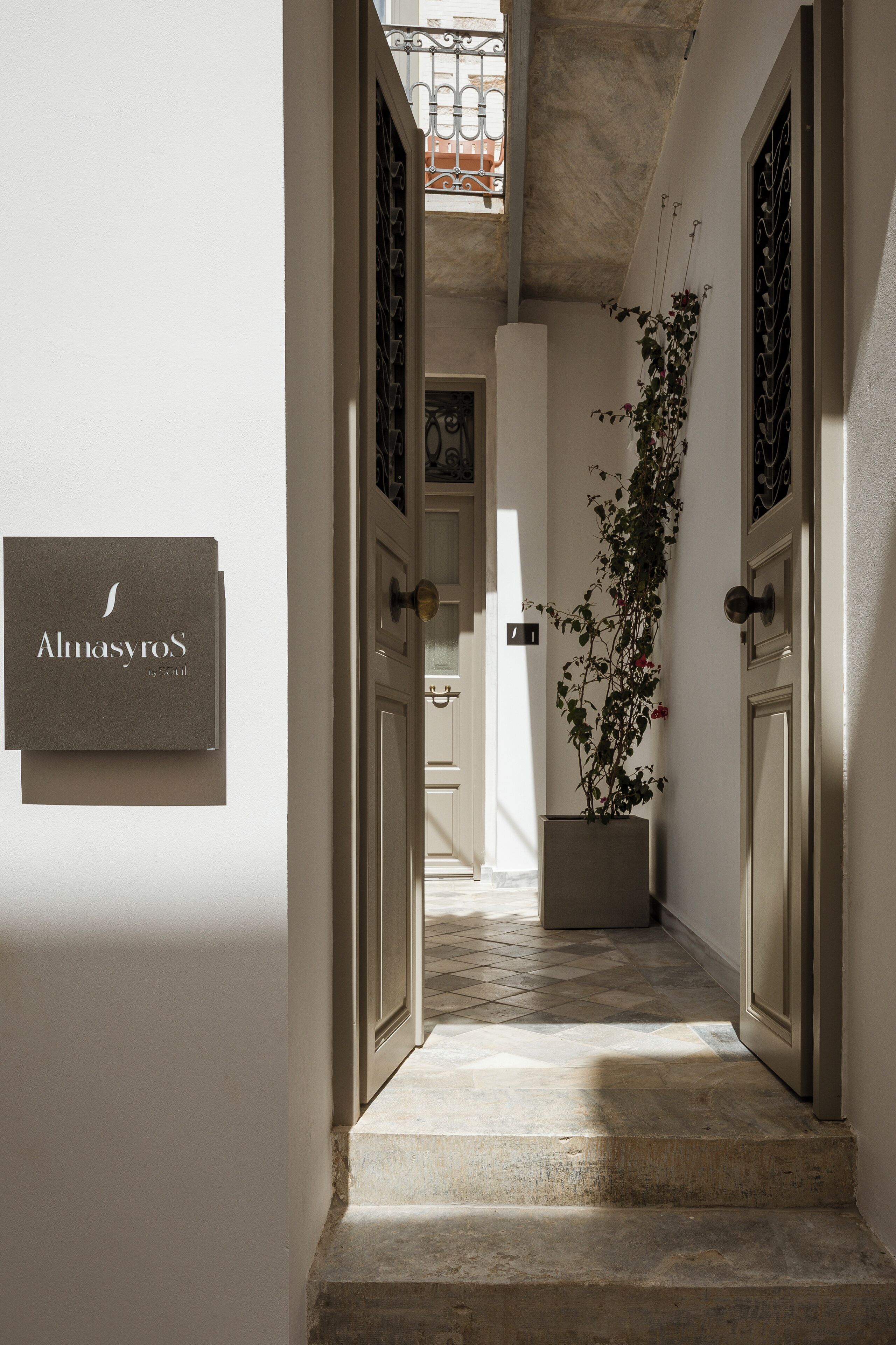 Un pasillo con un cartel que dice "Alnasyros", una planta en maceta y un piso de baldosas.