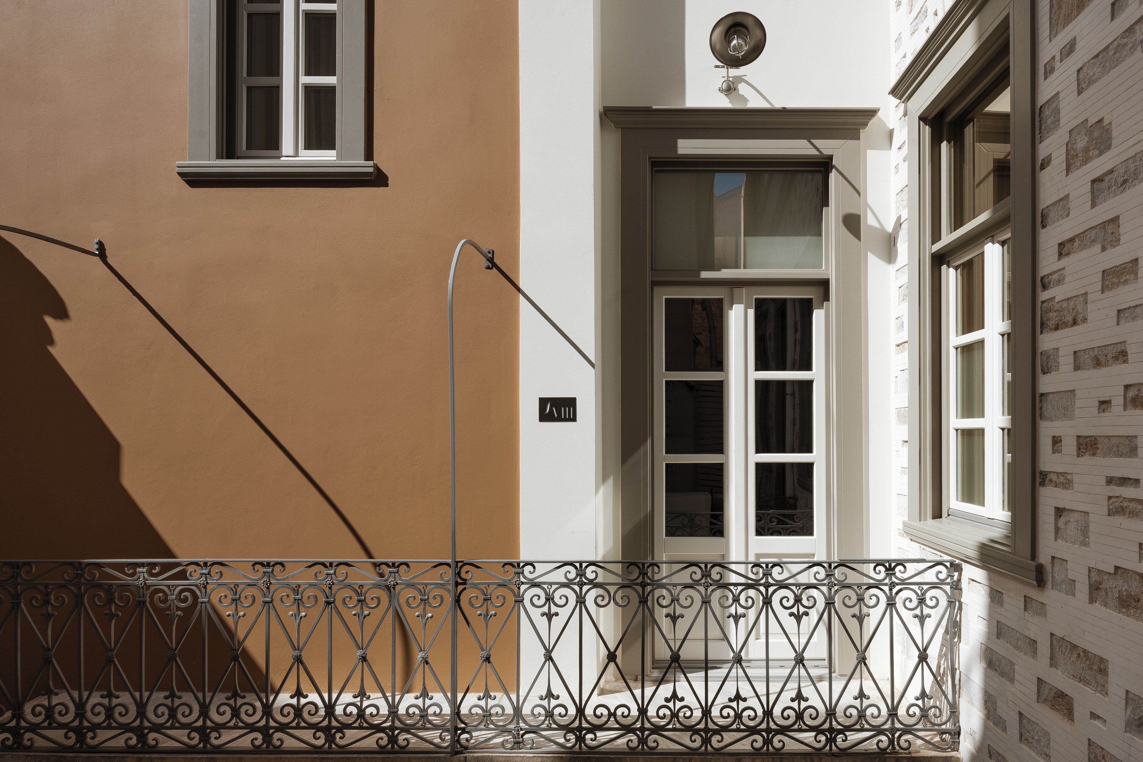 Fachada de edificio con una combinación de colores marrón y blanco, una puerta blanca con paneles de vidrio y barandilla de balcón de metal.